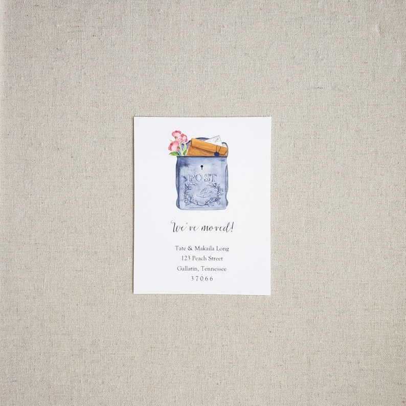 May include: A watercolor illustration of a blue mailbox with a keyhole and the word "POST" on the front. The mailbox is overflowing with letters and envelopes. Pink flowers are peeking out from the top of the mailbox. The text "We've moved!" is written in cursive below the mailbox, followed by the new address: Tate & Makaila Long, 123 Peach Street, Gallatin, Tennessee 37066.