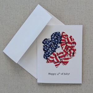 May include: A greeting card with a wreath made of red, white, and blue ribbon bows. The ribbon is patterned with stars and stripes. The text on the card reads "Happy 4th of July!"