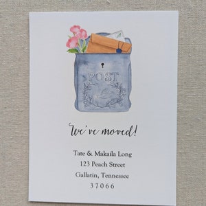 May include: A watercolor illustration of a blue mailbox with a brown envelope and pink flowers sticking out of the top. The mailbox has the word "POST" written on it. The text "We've moved!" is written below the mailbox, followed by the address "Tate & Makaila Long, 123 Peach Street, Gallatin, Tennessee 37066".