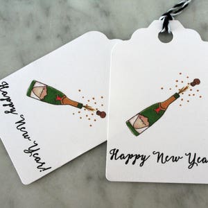 May include: Two white gift tags with a black and white string. Each tag has a drawing of a champagne bottle popping with the text "Happy New Year!"