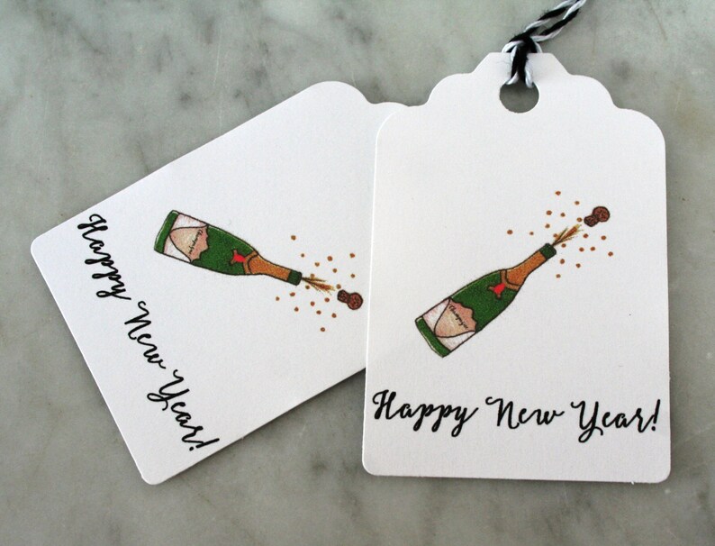May include: Two white gift tags with a black and white string. Each tag has a drawing of a champagne bottle popping with the text "Happy New Year!"