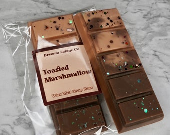 May include: Two brown wax melt snap bars with a light brown and dark brown swirl pattern and glitter. The bars are packaged in a clear plastic bag with a label that reads "Breonia Lafave Co. Toasted Marshmallow Wax Melt Snap Bars".