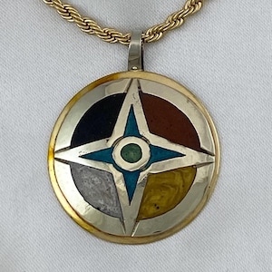 May include: A gold chain necklace with a round pendant featuring a four-pointed star with a turquoise center. The star is surrounded by four sections of different colored stones: black, brown, white, and yellow.