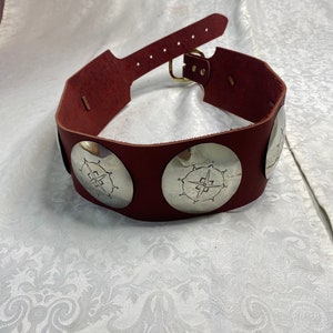 May include: A burgundy leather belt with silver circular buckles featuring a compass design.