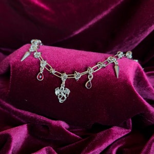 May include: A silver chain bracelet with a dragon charm and red gemstone accents. The bracelet has spikes on the chain.