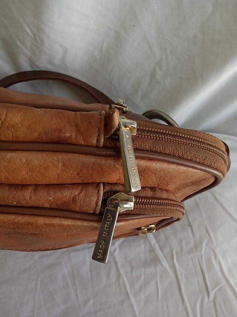 Puede incluir: Un bolso bandolera de cuero marr&oacute;n con m&uacute;ltiples compartimentos y cierre de cremallera. El bolso tiene una correa para el hombro y tiradores de cremallera met&aacute;licos. Los tiradores de la cremallera tienen la inscripci&oacute;n "MADE IN ITALY".