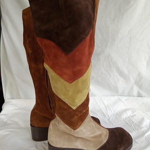 May include: Knee-high suede boots in shades of brown, tan, and rust. The boots feature a chevron design on the front, a rounded toe, and a block heel. The boots are a vintage style.