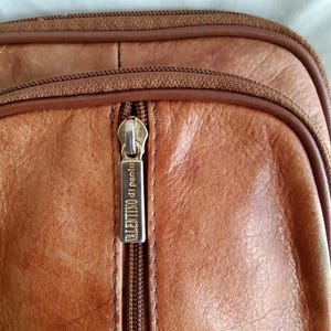 Puede incluir: Primer plano de un bolso de cuero marr&oacute;n con cremallera. El tirador de la cremallera tiene el texto "VALENTINO di paolo". El bolso tiene una superficie texturizada y una cremallera marr&oacute;n.