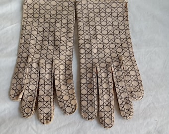 Op de afbeelding: Een paar beige handschoenen met een donkerbruin ruitpatroon van elkaar kruisende lijnen en cirkels. De handschoenen hebben een standaard ontwerp met vijf vingers, gestikte naden langs de randen en een rechte polsboord.