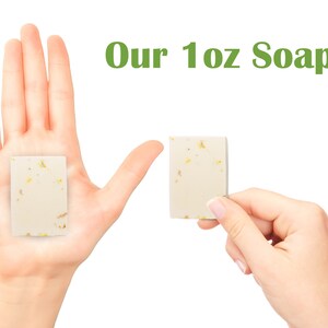 Pu&ograve; includere: Due mani che tengono una saponetta da 1 oncia. Il sapone &egrave; bianco con macchie dorate. Il testo "Our 1 oz Soap" &egrave; scritto in verde sopra le mani.