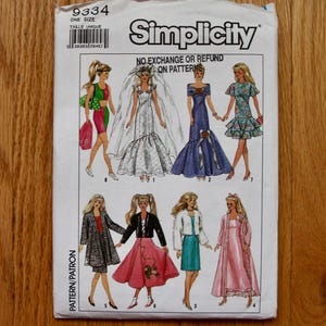 May include: A Simplicity sewing pattern packet with illustrations of doll dresses. The packet includes the number 9334 and the text "ONE SIZE". The designs include a wedding dress, evening gowns, and casual outfits.