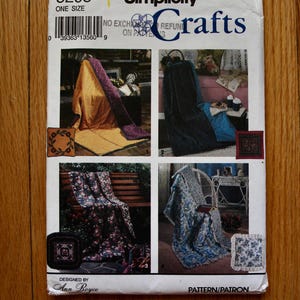 May include: A Simplicity Crafts sewing pattern envelope, number 8208, designed by Ann Boyce. The white paper envelope features four distinct photographic examples of quilted blankets and matching square pillows in various floral and solid fabric designs.