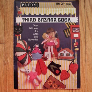 May include: A vintage book titled "Third Bazaar Book" with a yellow and white striped cover. The book features a variety of knitted items, including a doll, a house, a cat, a rabbit, and a pair of mittens. The book cover also includes the text "Over 40 ideas for Gifts and Novelties".