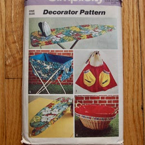 Peut inclure: Un paquet de patrons de décorateur Simplicity vintage. Le paquet présente des images d'une planche à repasser florale, d'un panier à linge, d'un tablier avec des poches jaunes, d'une housse de planche à repasser rembourrée et d'un panier rouge.