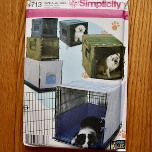 May include: A Simplicity 4713 sewing pattern envelope for pet crate covers. The packaging features illustrations of various dogs inside wire crates with fabric covers in blue, green, and grey, along with paw print graphics and text.