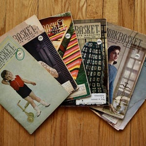 May include: A collection of six vintage Workbasket and Home Arts magazines from the 1960s, featuring various cover illustrations including a child with a toy, colourful striped patterns, knitted textiles, and portraits, all with printed price circles.