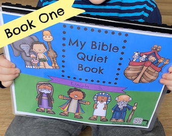 May include: A blue and green "My Bible Quiet Book" with the text "Book One" in a yellow banner. The cover features illustrations of animals, people, and the text "Lincoln S.". The book is held by a person.