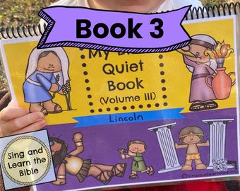 May include: A spiral-bound quiet book titled My Bible Quiet Book Volume III with a yellow and purple cover featuring cartoon illustrations of biblical figures, including a person with a slingshot and a person holding a torch, and the name Lincoln.