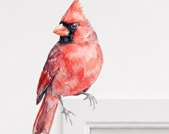 May include: Watercolor painting of a vibrant red cardinal bird with a black mask and beak. The bird is perched on a white surface, showcasing its detailed feathers and posture. The artwork captures the bird's natural beauty.