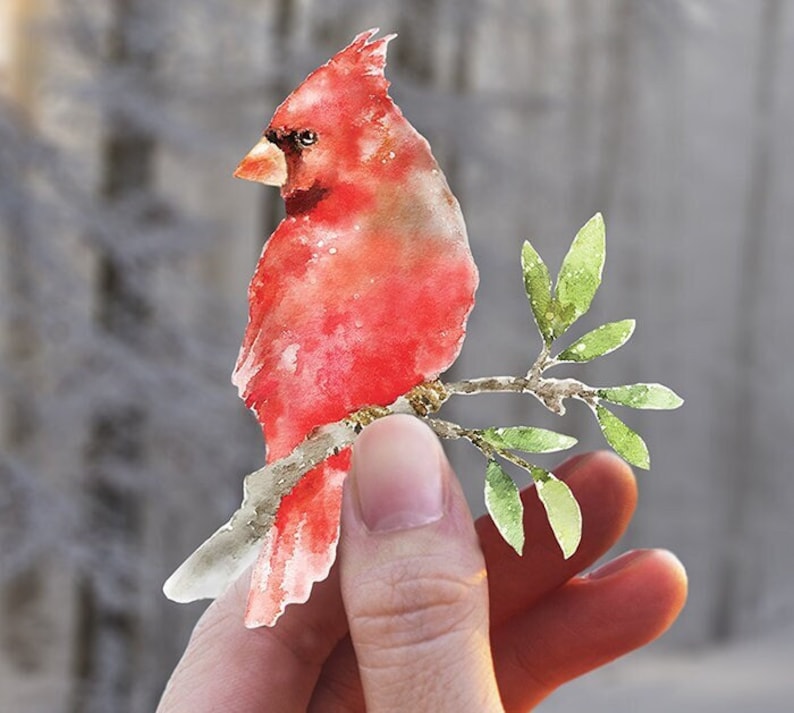 Pu&ograve; includere: Un dipinto ad acquerello di un cardinale rosso appollaiato su un ramo con foglie verdi. L'uccello &egrave; dipinto in uno stile realistico con dettagli delicati.