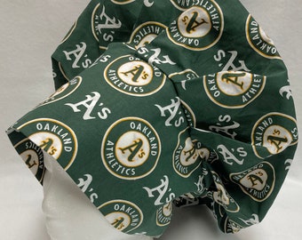 May include: Green fabric scrub hat with a repeating pattern of white "Oakland A's" logos. The logo features a gold circle with the team's name and a stylized "A" inside.