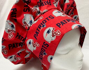 May include: Red scrub hat with a white and blue New England Patriots logo pattern. The hat has a gathered top and a tie at the back.
