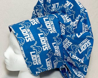 May include: A blue and white Detroit Lions bouffant scrub cap. The cap is patterned with the team's logo and the words "Detroit Lions" in white. The cap is designed to cover the hair and is worn in medical or food service settings.