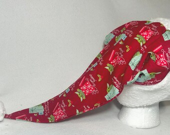 May include: Red and green Christmas hat with a white pom-pom and a pattern of Baby Yoda characters holding presents. The hat has a long, pointed tip and is made of fabric.