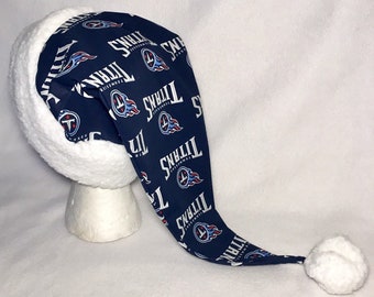 May include: A blue and white Santa hat with a white pom-pom on the end. The hat is decorated with a repeating pattern of the Tennessee Titans logo and the words "TITANS" and "NASHVILLE".