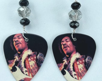 May include: A pair of earrings featuring a guitar pick with a photo of Jimi Hendrix playing guitar. The guitar pick is black with a silver trim. The earrings are accented with black and clear beads.