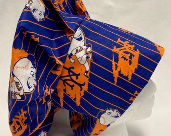 May include: A blue and orange fabric chef hat with a striped pattern and a repeated image of a cartoon baseball player wearing a Mets jersey. The hat is on a white mannequin head.
