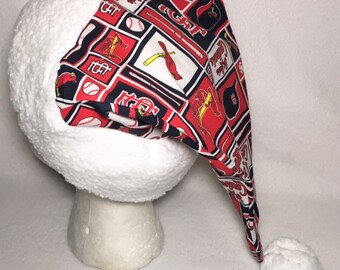 May include: A white and red Santa hat with a St. Louis Cardinals pattern. The hat has a white pom-pom on the end.
