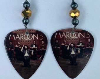 May include: A pair of guitar pick earrings featuring a photo of the band Maroon 5. The earrings are made with silver beads and gold beads.