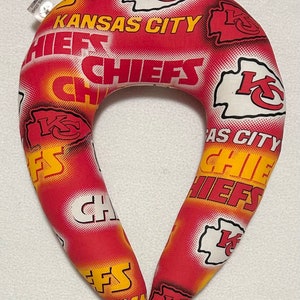 May include: A red, white, and yellow travel pillow with the Kansas City Chiefs logo and team name repeated on the fabric.