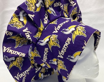 May include: A purple and gold scrub cap featuring the Minnesota Vikings logo and the word "Vikings" in white. The cap is made of fabric and is designed to cover the hair. The cap is shown on a white mannequin head.