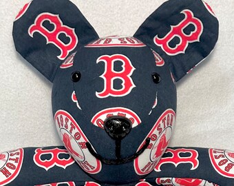 May include: A handmade plush bear with a navy blue fabric patterned with the Boston Red Sox logo in red and white. The bear has black button eyes and a black stitched nose. The bear's ears and body are covered in the team's logo.
