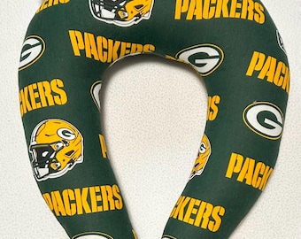 May include: Green and gold travel pillow with a repeating pattern of the Green Bay Packers logo, including the team name and a football helmet.