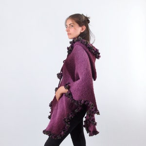以下が含まれることがあります： フリルトリムが付いた紫色のフード付きニットポンチョ。ポンチョは柔らかくふわふわの糸でできており、ゆったりとしたフィット感です。