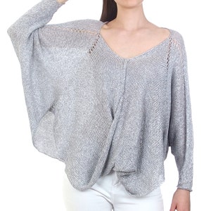 May include: A gray knit sweater with a V-neck and long sleeves. The sweater has a loose, flowing fit.