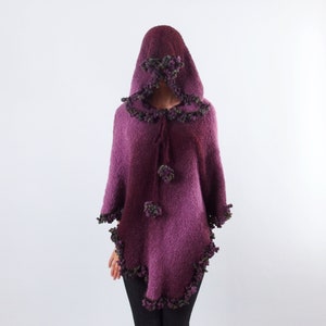以下が含まれることがあります： 濃い色から薄い色へのグラデーションで染められた、紫色のフード付きポンチョ。ポンチョはフリンジの縁取りと、ネックラインに沿ってポンポンが付いています。