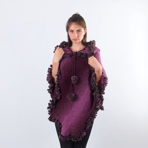 以下が含まれることがあります： フリンジトリムが付いた、テクスチャニットの紫色のフード付きポンチョ。ポンチョは首にドローストリングクロージャーが付いています。