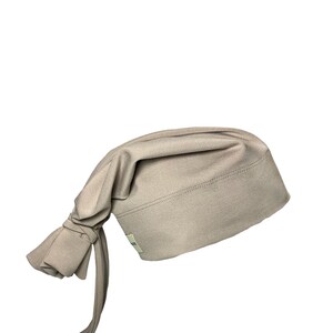 May include: A light brown fabric chef hat with a long tie. The hat is made of a soft, stretchy material and has a simple design.