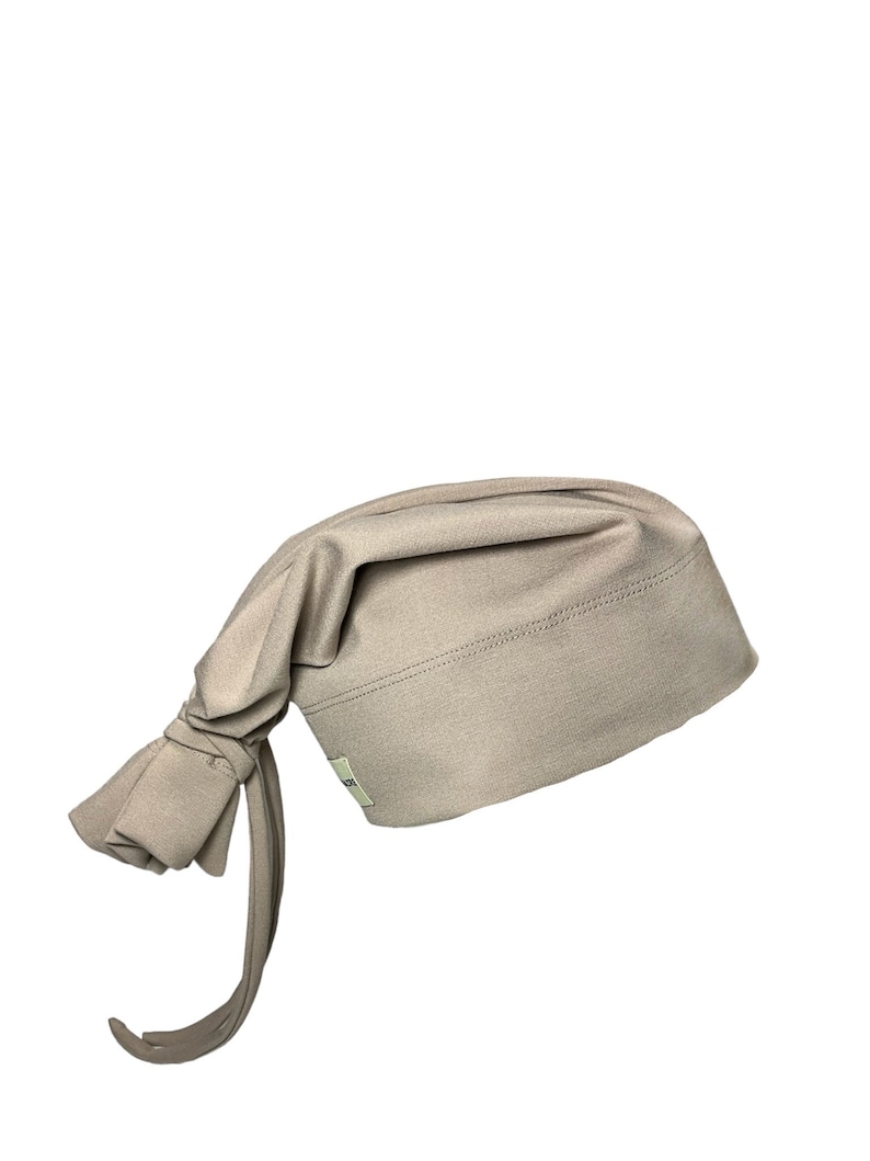 May include: A light brown fabric chef hat with a long tie. The hat is made of a soft, stretchy material and has a simple design.