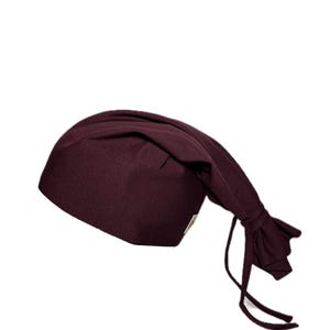 Puede incluir: Un gorro quirúrgico burdeos con cierre de lazo anudado. El gorro está hecho de una tela suave y está diseñado para ser usado en un entorno médico o profesional. El gorro es de color liso y tiene un diseño sencillo y funcional.