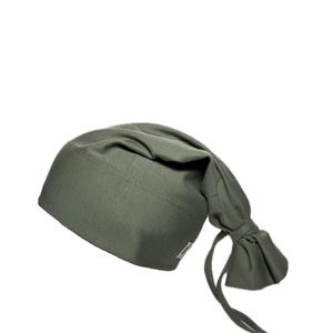 Könnte beinhalten: Olivgrüne Schlafhaube mit geknotetem Schwanz und angenähten Bändern. Die Haube ist aus einem weichen Stoff gefertigt und hat ein kleines Etikett an der Seite. Zum Schlafen konzipiert.