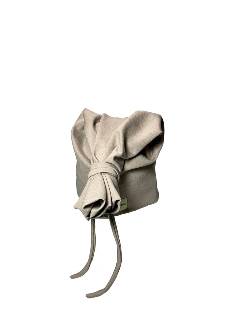 May include: A beige knit hat with a bow on top and two long ties. The hat has a small label with the word "SRE" on it.
