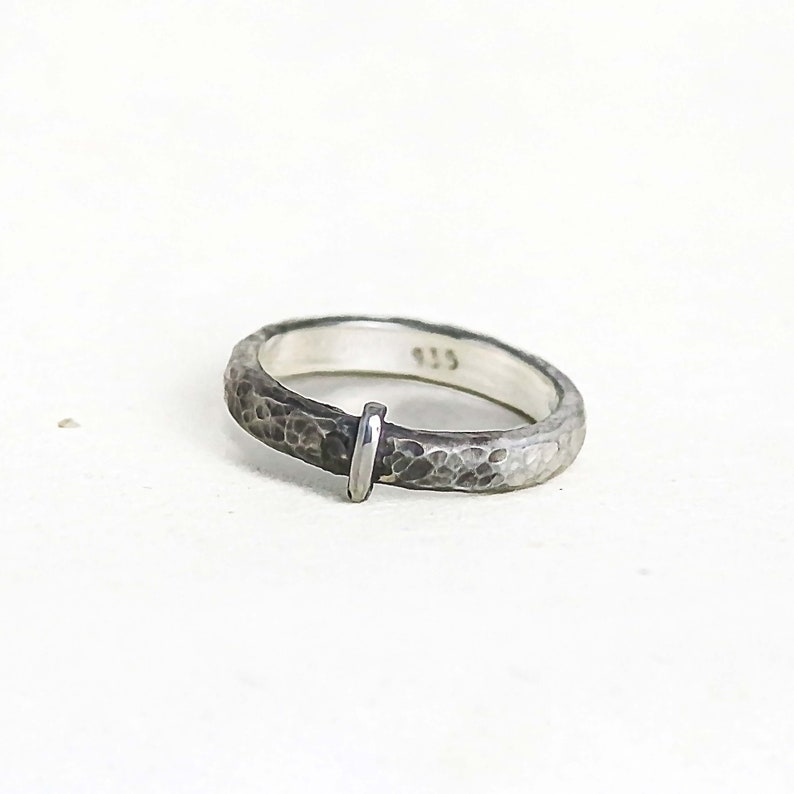 Blacksmith-inspired band with hammered details and a polished vertical bar. The front of the ring is antiqued with patina for depth and dimension