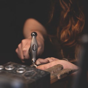 a woman hand forges a sterling silver ring band. This photo was taken of the owner, showing that we actually hand craft our pieces at Skolland Jewelry. Each piece is made one at a time in small batches. 100% USA made, ethical craftsmanship.