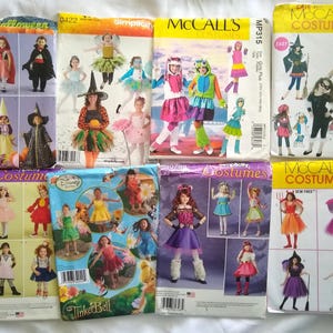 May include: A collection of eight sewing pattern envelopes for children's costumes, featuring various designs including witches, fairies, superheroes, and animals, with printed illustrations of models wearing the finished garments on each package.