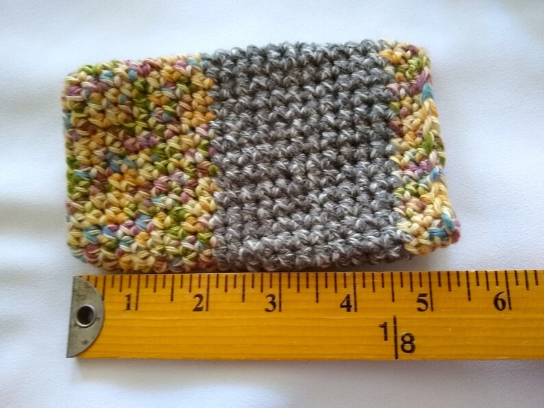 May include: A crocheted gray and multi-colored coaster with a textured surface. The coaster measures approximately 4 inches wide.